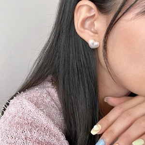 Close-up of heart-shaped pearl earrings worn by a model in a minimalist style