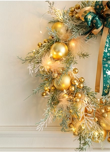 Detail of Christmas wreath featuring golden ornaments, feathers, green ribbons and LED lights