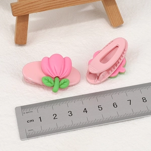 Detail view of pink tulip hair clips measured with a ruler on white fabric background