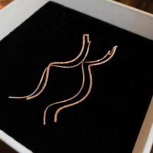 Close-up of rose gold minimalist wave tassel earrings on black velvet background