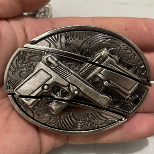 Close-up of vintage zinc alloy belt buckle featuring embossed crossed handguns and 2000 mark