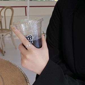 Close-up of minimalist silver adjustable ring worn on finger in a chic cafe setting