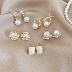 Close-up of pearl and rhinestone earrings collection on champagne silk fabric background