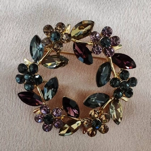 Exquisite gold floral wreath brooch with colorful crystals on a soft pink textile background