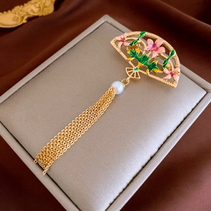 Détail d'une broche en éventail doré avec fleurs en émail rose et longs glands de chaîne