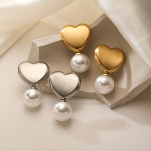 Elegant 18K gold and silver heart pearl stud earrings on a textured stone surface