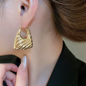 Close-up of golden textured hoop earrings with wavy metal pattern on a female model
