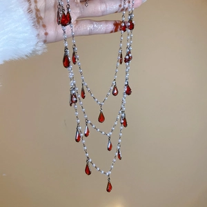 Detail showing triple-layer silver necklace with red teardrops and white pearls