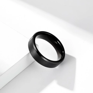 Minimalist matte black brushed tungsten steel ring for men on a white geometric block