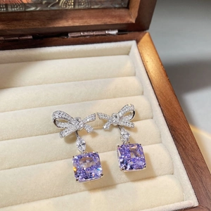 Macro shot of silver bow stud earrings with square purple zircon on white velvet box