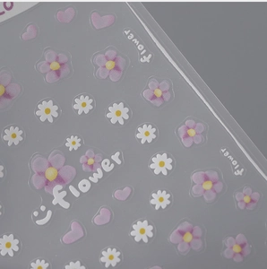 Close-up of 3D embossed floral nail stickers featuring purple flowers and pink hearts