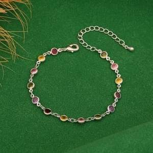 Detailed shot of silver-tone bracelet with colorful cubic zirconia on green background