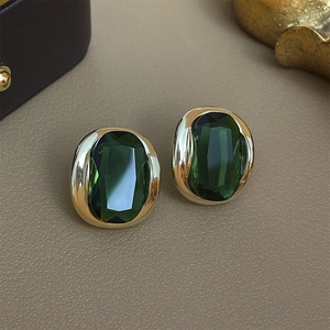 Close-up of vintage gold-plated earrings with emerald green oval zircon on leather