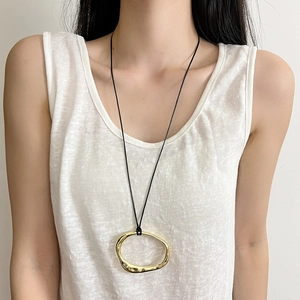 Detail of minimalist irregular golden pendant necklace with hammer texture on black cord