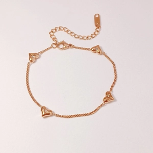 Detailed close-up of a rose gold heart bracelet with small diamonds on a beige surface