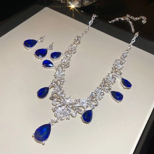 Detailed flat lay of silver necklace and earrings set with blue teardrop stones