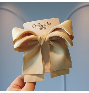 Detail of a champagne satin bow hair clip with tiered silk ribbon on a white card