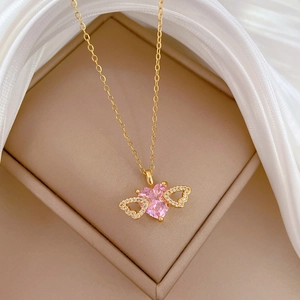 Detailed macro of golden heart necklace with pink stone and diamond wings in gift box