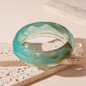 Close-up of green marble-patterned acrylic bangle resting on a travertine stone