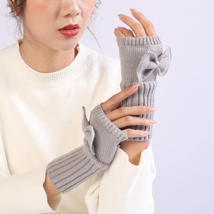 Detail of grey knitted fingerless gloves with bow accent on a soft white sweater sleeve