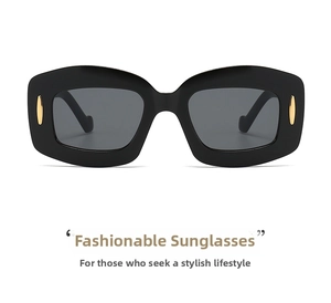 Close-up of black wide-frame sunglasses with dark lenses and gold oval side accents