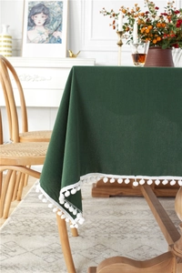 Detailed view of dark green washed cotton tablecloth featuring white pompom ball fringe trim