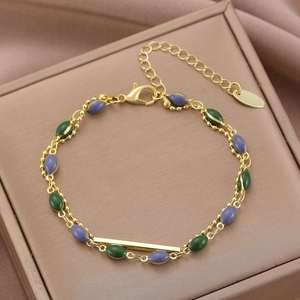 Dettaglio del bracciale dorato a doppio strato con perline verdi e viola su scatola