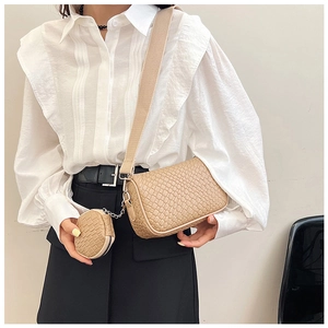 Detail view of beige woven crossbody bag with round charm pouch worn by model