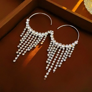 Détail de boucles d'oreilles créoles argentées avec de longues franges en strass