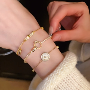 Close-up of stacked gold bamboo bracelets with zircon and flower charm on model wrist