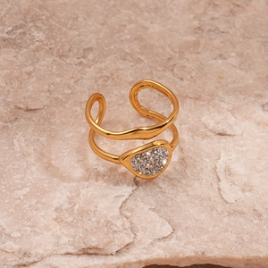 Detail of a double-layered gold ring with a sparkling rhinestone heart on a stone surface