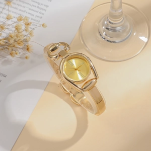 Close-up of golden bangle watch with Roman numerals and sunray dial on books