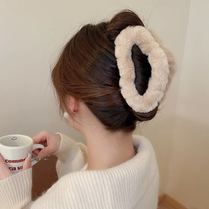 Close-up of beige plush faux fur claw clip on a woman's hair for autumn winter style