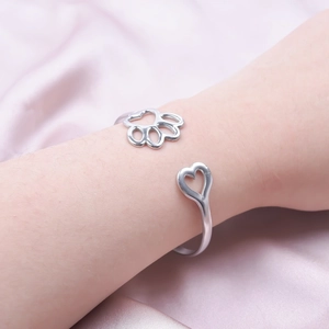 Close-up of adjustable silver open bangle featuring hollow heart and cute animal paw charms