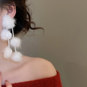 Close-up of elegant white pompom and crystal tassel earrings worn by a model