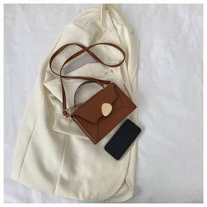 Detail of a brown patchwork handbag featuring a golden geometric buckle on an ivory blazer