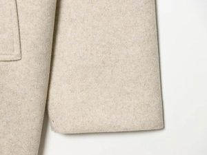 Nahaufnahme der eleganten beigen Wollstofftextur und der Nähte des Mantels im Detail