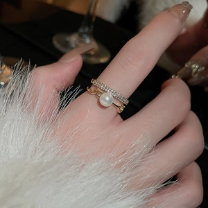 Dettaglio anello dorato a più strati con perle, cristalli e lettera B sulla mano