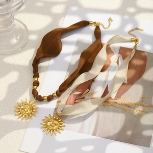 Detail of 18K gold sun pendant necklaces with brown and cream silk fabric ribbons