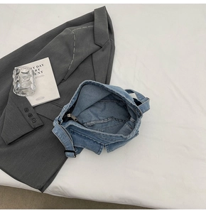 Detail of blue denim crossbody bag with adjustable shoulder strap and black zipper closure