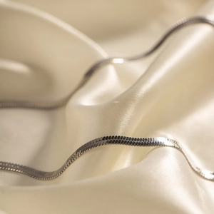 Macro detail of silver stainless steel snake bone chain on luxury cream silk fabric