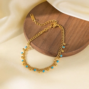 Golden chain necklace with sky blue beads and round charms on a walnut display tray
