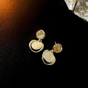 Detailed close-up of golden metallic hoop earrings with oval cat-eye stone on black background