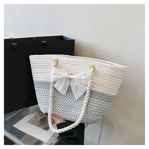 Detail showing hand holding a woven tote bag with a white bow and gradient texture
