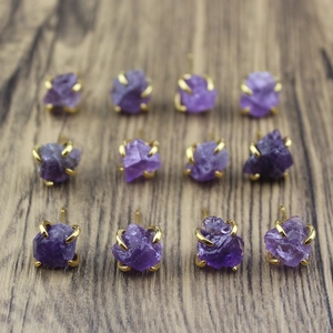 Macro view of raw amethyst stud earrings with gold four-claw settings on wood background