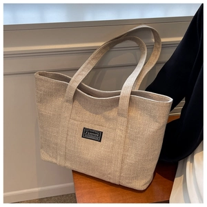 Detail of a beige canvas tote bag with fashion label on a wooden stool in a soft room