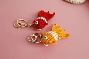 Detail of red and yellow handmade crochet goldfish keychains on a soft pink background