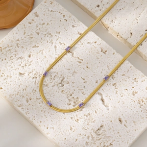 Close-up of gold snake chain necklace with purple rectangular zircons on white rock