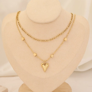 Detail of layered gold stainless steel necklace with heart pendant on model