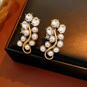 Detailed view of S-shaped vintage gold earrings featuring white pearls and clear crystals